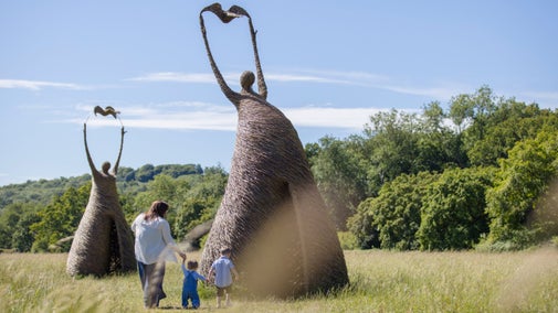 Mum and two small children walking toward large willow sculptures in meadow at Runnymede